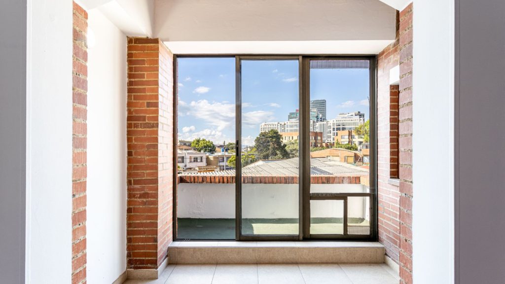A room with a large window in need of glass replacement overlooking a city.