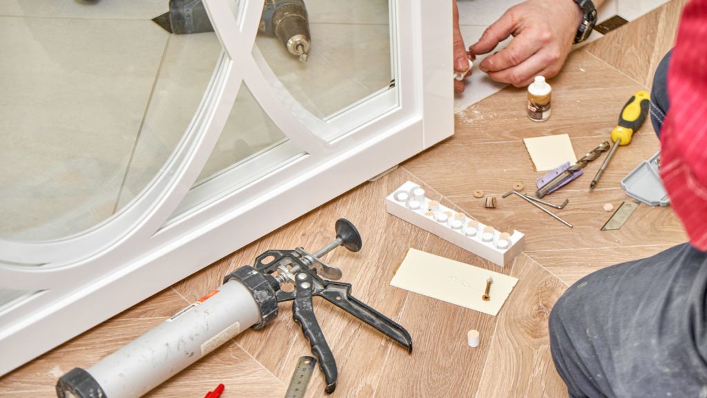 A man is repairing a sliding door on a wooden floor with tools.